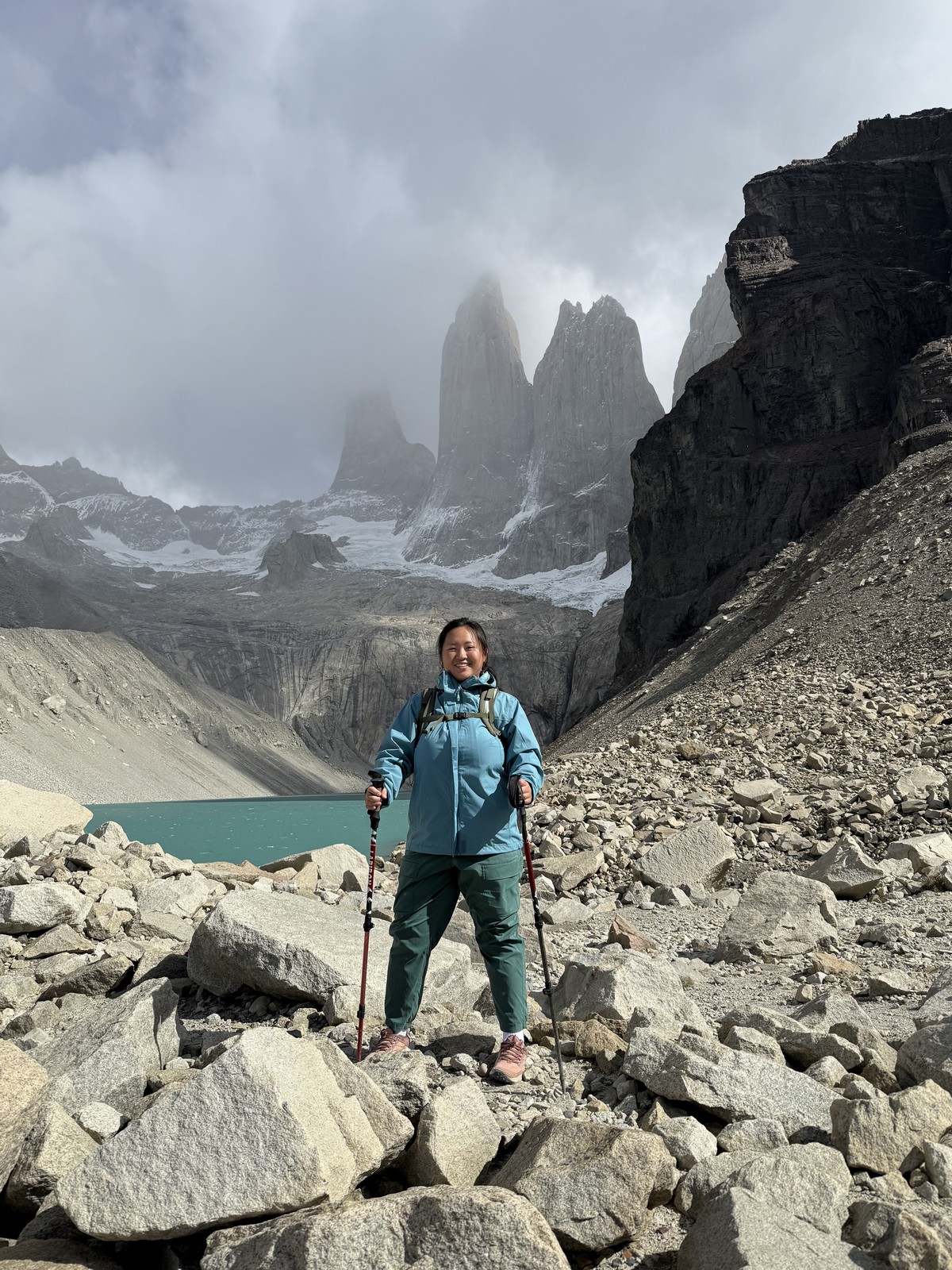 A hiker on rocky terrain beneath misty mountain peaks.