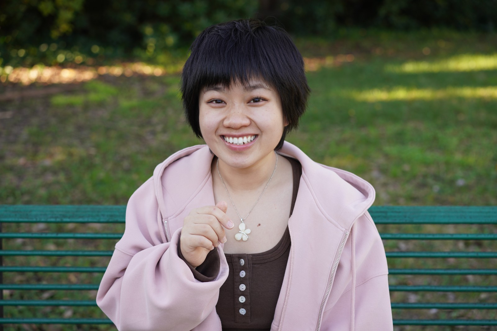 A smiling person sitting on a green park bench.