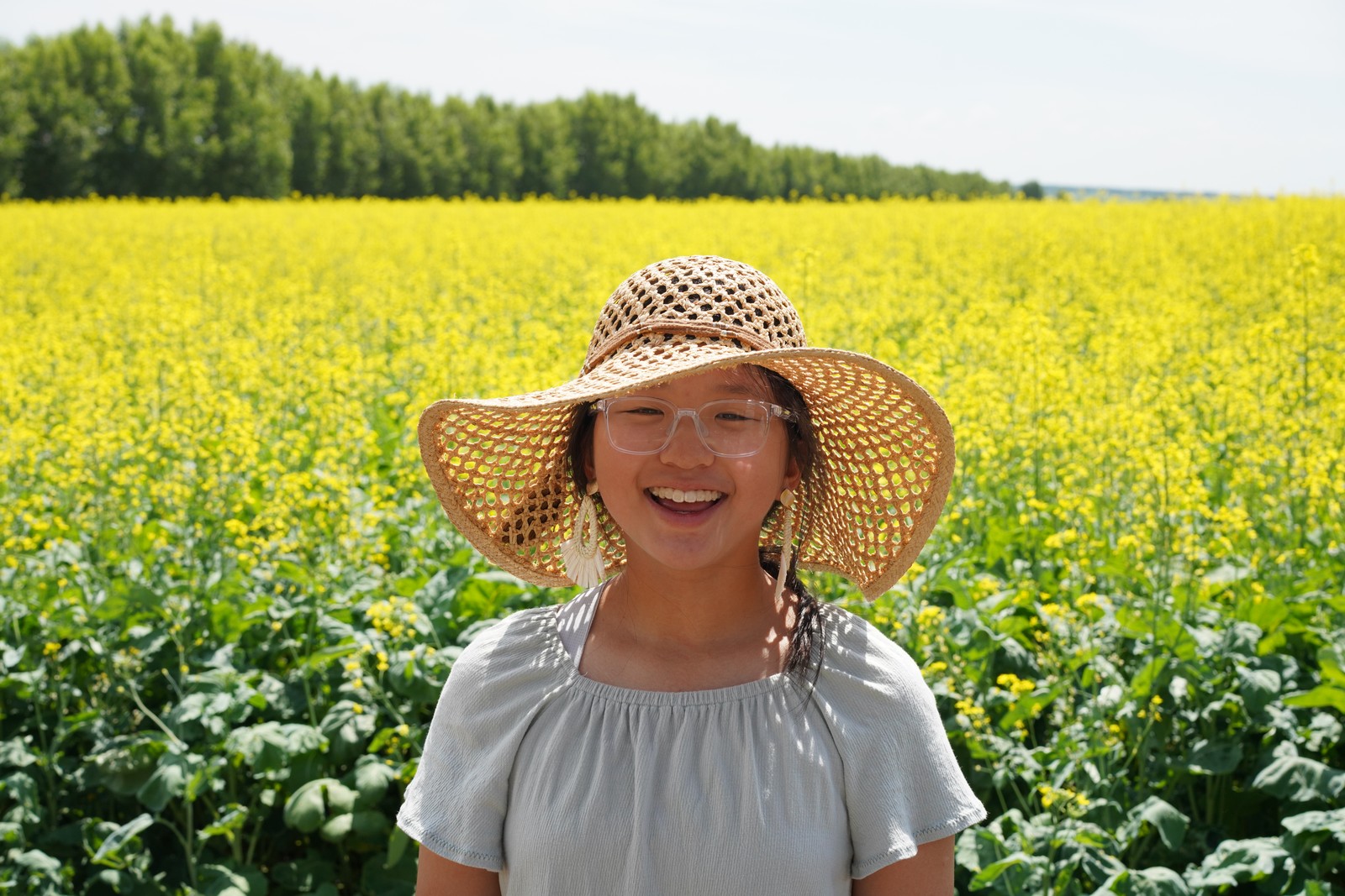 A smiling person in a straw hat amid yellow flowers.