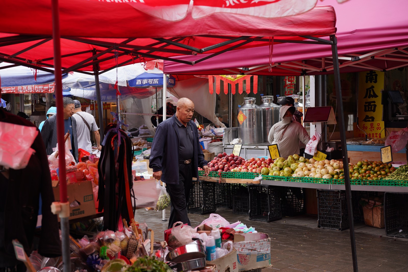 People shopping beneath red market canopies.